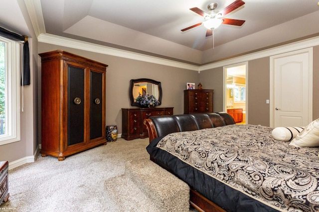 bedroom featuring multiple windows, a tray ceiling, ensuite bath, and ceiling fan