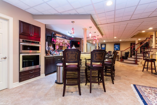 bar featuring a drop ceiling, double oven, pendant lighting, and ornate columns