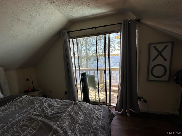 bedroom featuring wood-type flooring, a textured ceiling, access to exterior, lofted ceiling, and a water view