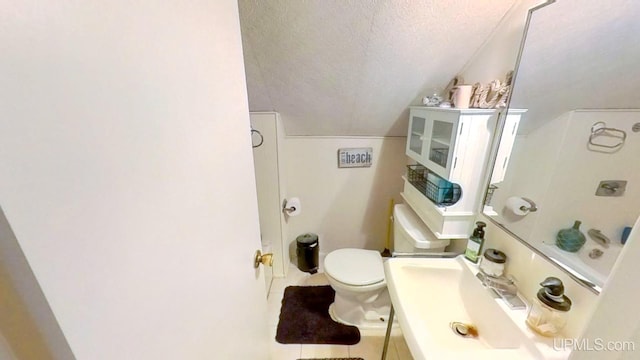 bathroom featuring vanity, toilet, a textured ceiling, tile patterned floors, and vaulted ceiling