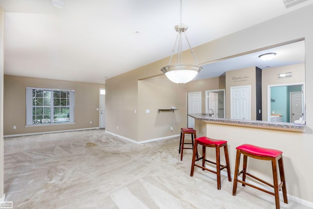 kitchen with a kitchen bar, light colored carpet, decorative light fixtures, and sink