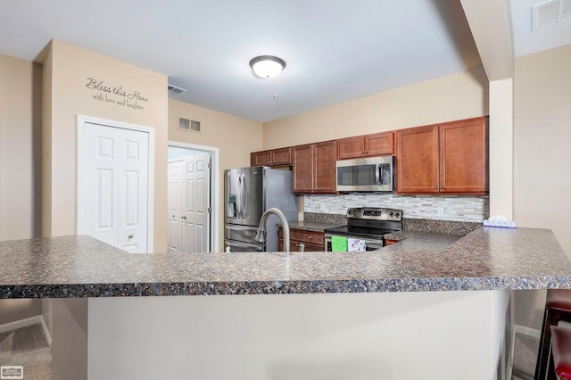 kitchen with sink, kitchen peninsula, backsplash, appliances with stainless steel finishes, and a kitchen breakfast bar