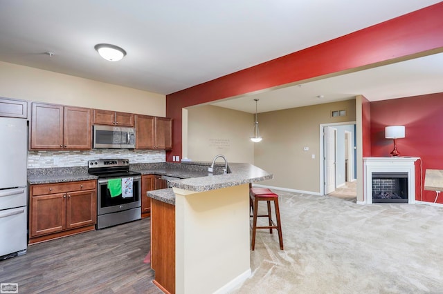 kitchen featuring dark hardwood / wood-style floors, a kitchen bar, hanging light fixtures, backsplash, and appliances with stainless steel finishes