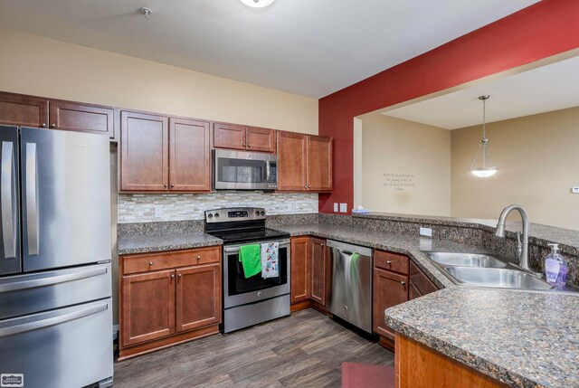 kitchen featuring pendant lighting, kitchen peninsula, sink, stainless steel appliances, and dark hardwood / wood-style flooring