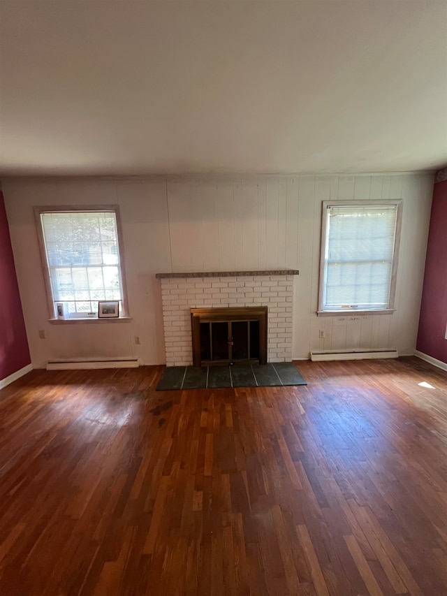 unfurnished living room featuring a brick fireplace, dark hardwood / wood-style floors, and a baseboard heating unit