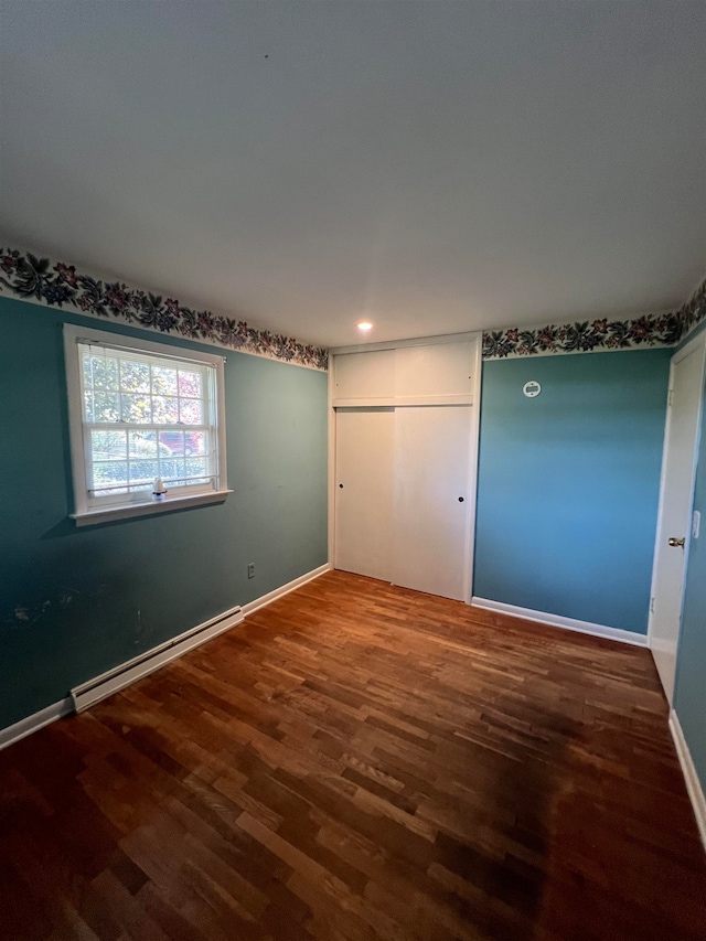 unfurnished bedroom featuring a baseboard radiator, wood-type flooring, and a closet