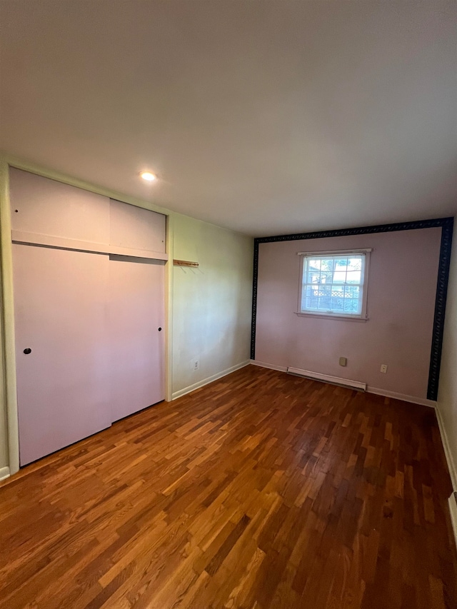 unfurnished bedroom featuring a closet, baseboard heating, and hardwood / wood-style flooring