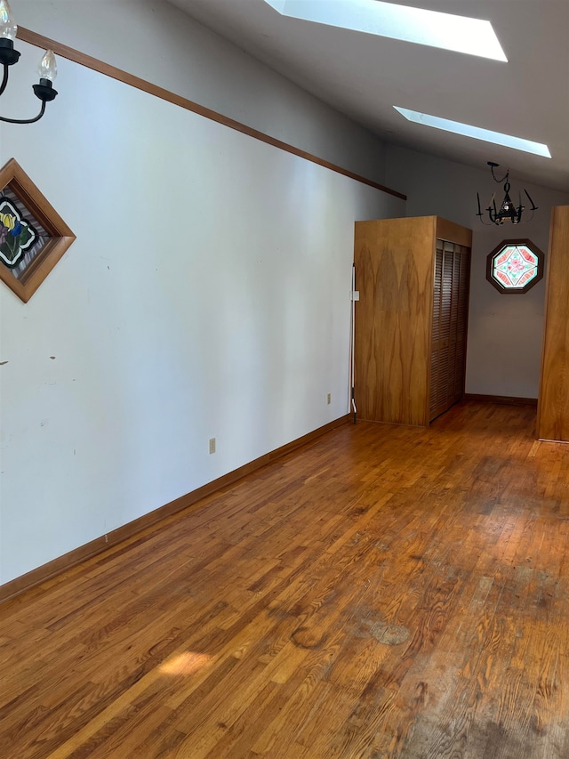 empty room featuring an inviting chandelier, dark wood-type flooring, and a skylight