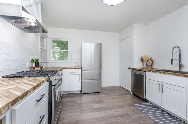 kitchen featuring white cabinets, sink, wall chimney exhaust hood, light hardwood / wood-style flooring, and stainless steel appliances