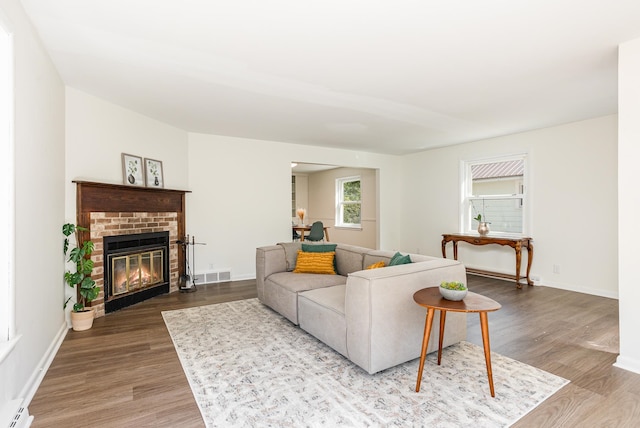 living room featuring wood-type flooring, baseboard heating, and a brick fireplace