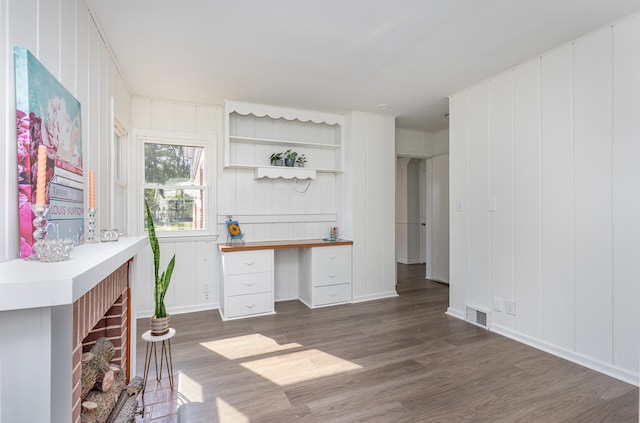 home office with a brick fireplace, built in desk, and dark hardwood / wood-style flooring