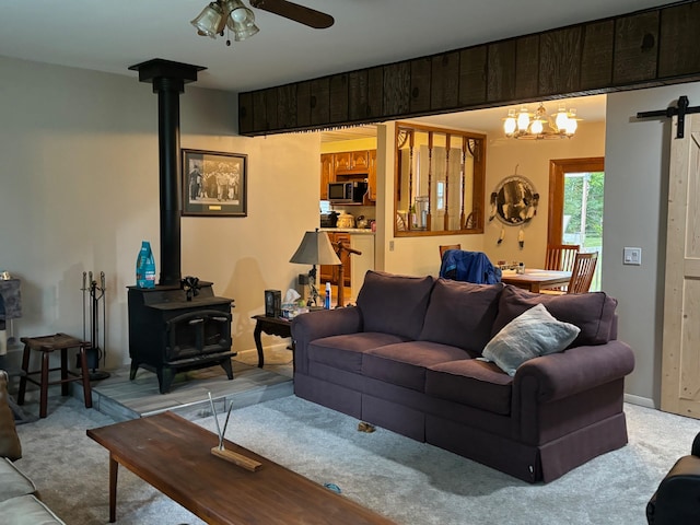 living room with a wood stove, a barn door, light colored carpet, and ceiling fan