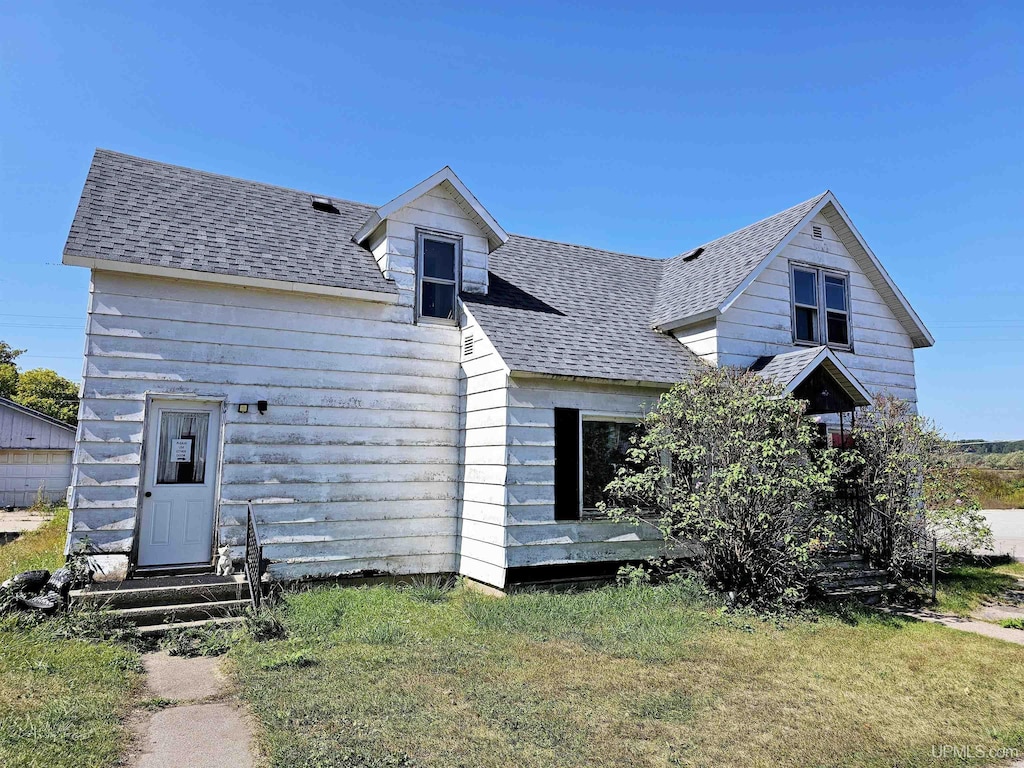 view of front of home featuring entry steps, a shingled roof, and a front lawn