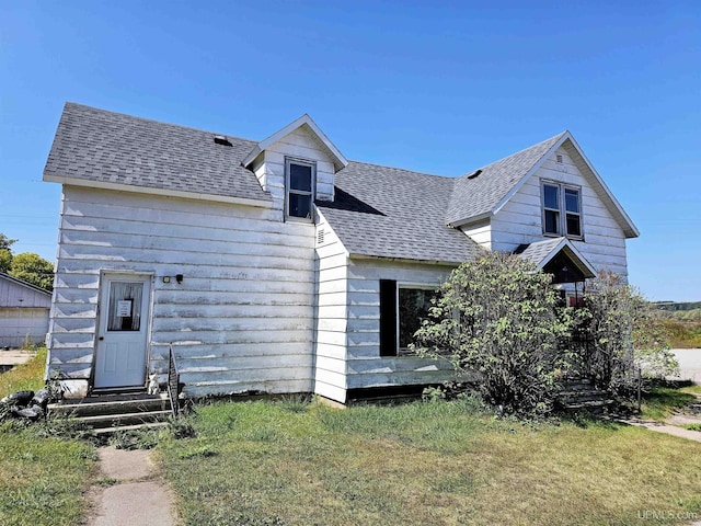 view of front of home featuring entry steps, a shingled roof, and a front lawn