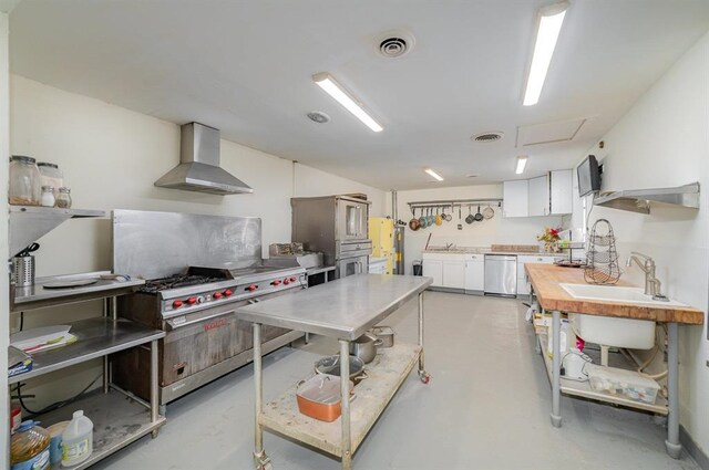 kitchen featuring stainless steel appliances, white cabinetry, wall chimney range hood, and sink