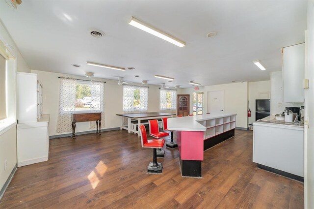 kitchen featuring a breakfast bar, a center island, black fridge, dark wood-type flooring, and white cabinetry