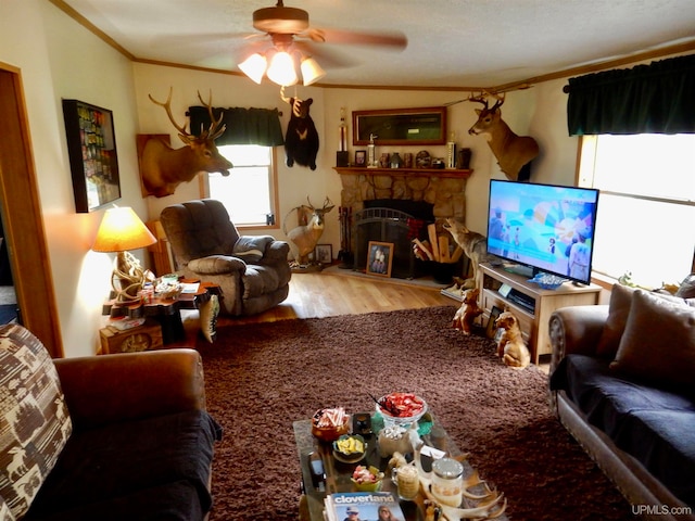 living room with ceiling fan, a stone fireplace, crown molding, and hardwood / wood-style floors