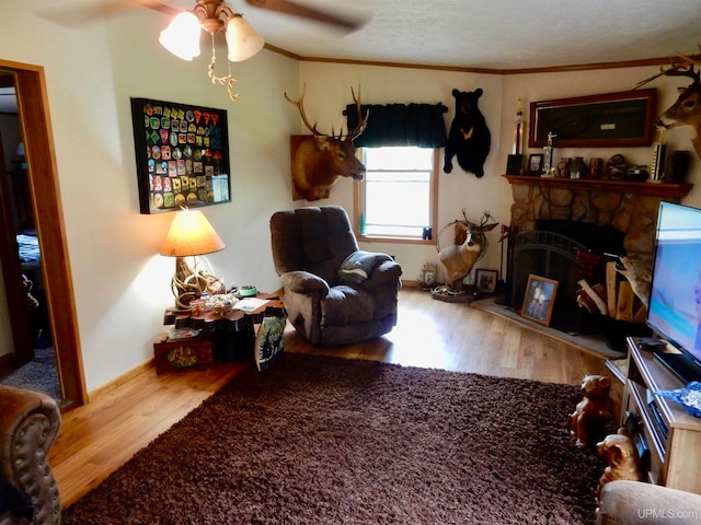 living room featuring a fireplace, a textured ceiling, wood-type flooring, ceiling fan, and ornamental molding