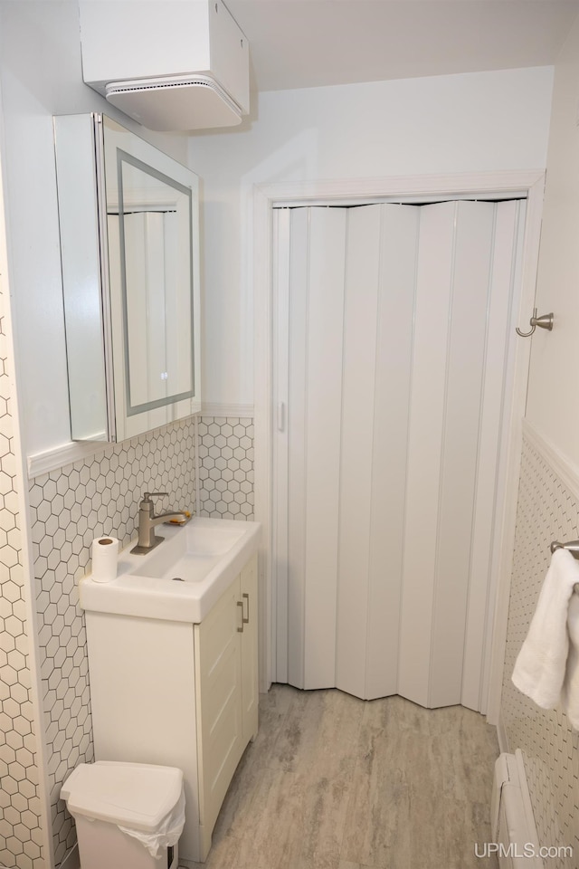 bathroom with tile walls, vanity, baseboard heating, hardwood / wood-style flooring, and toilet