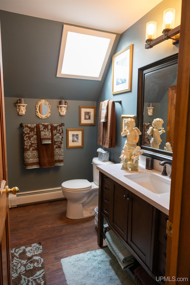 bathroom with vanity, toilet, lofted ceiling with skylight, a baseboard radiator, and hardwood / wood-style floors