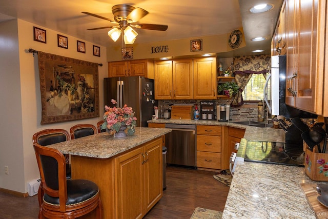 kitchen with light stone counters, ceiling fan, stainless steel appliances, dark hardwood / wood-style floors, and a kitchen breakfast bar