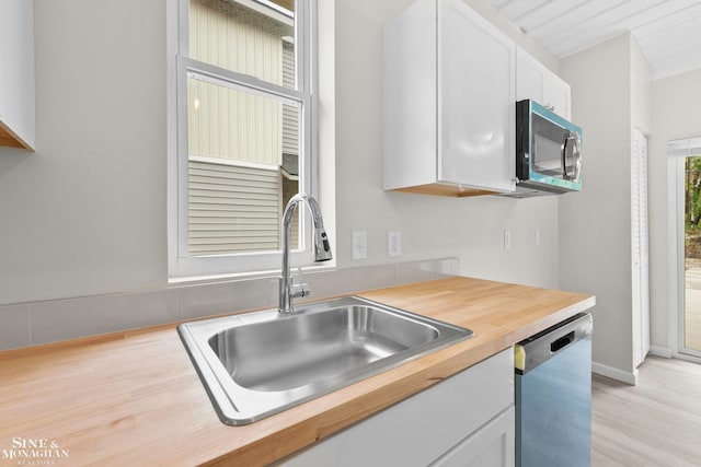 kitchen with stainless steel appliances, white cabinets, wooden counters, sink, and light hardwood / wood-style floors