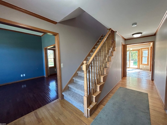 staircase featuring wood-type flooring, ornamental molding, and plenty of natural light