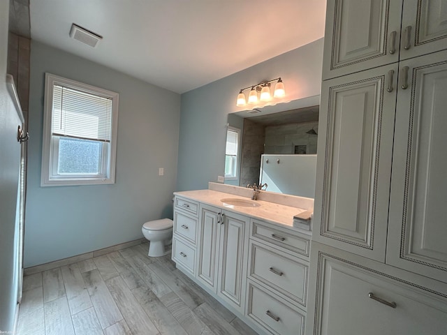 bathroom featuring wood-type flooring, a tile shower, vanity, and toilet