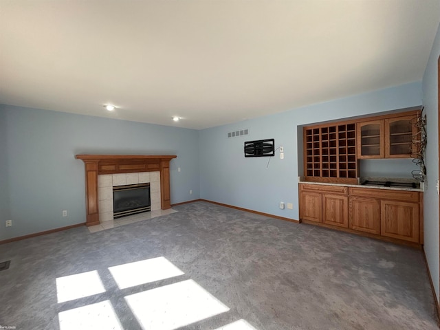 unfurnished living room with light colored carpet and a tiled fireplace