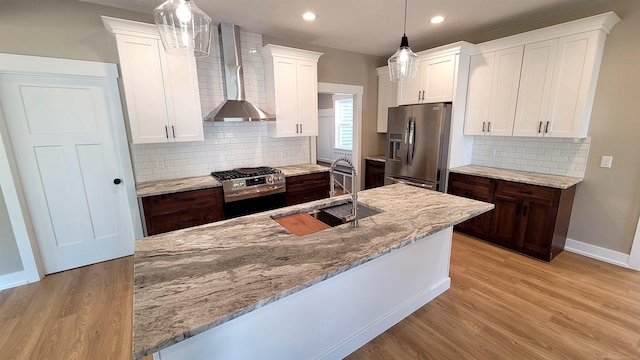 kitchen featuring sink, wall chimney range hood, hanging light fixtures, light hardwood / wood-style flooring, and appliances with stainless steel finishes