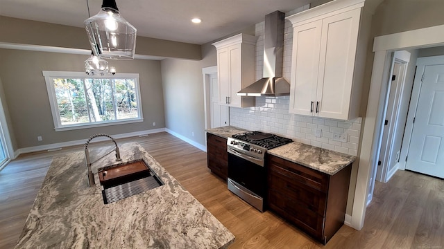 kitchen featuring stainless steel range with gas cooktop, wall chimney exhaust hood, decorative light fixtures, and white cabinets