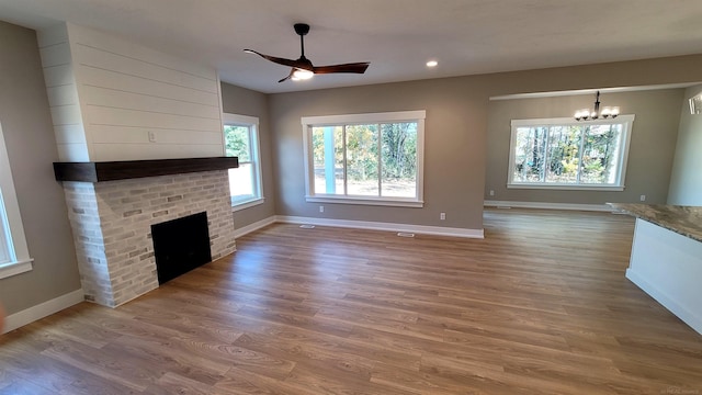 unfurnished living room featuring a brick fireplace, hardwood / wood-style flooring, and ceiling fan with notable chandelier