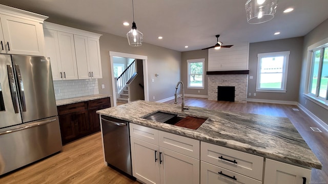 kitchen with sink, a brick fireplace, white cabinetry, appliances with stainless steel finishes, and light hardwood / wood-style floors