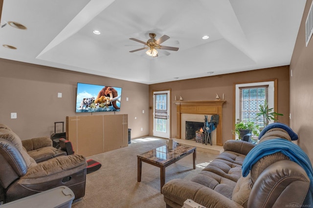 carpeted living room with a high end fireplace, ceiling fan, and a raised ceiling