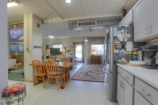 kitchen with a drop ceiling, decorative light fixtures, stainless steel fridge, and white cabinetry