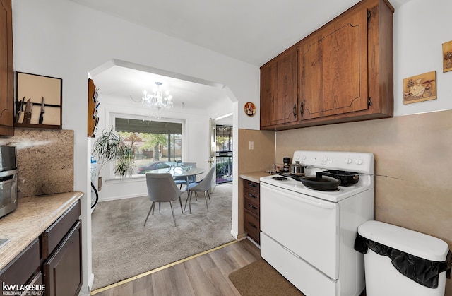 kitchen with white stove, decorative light fixtures, a chandelier, and light hardwood / wood-style flooring