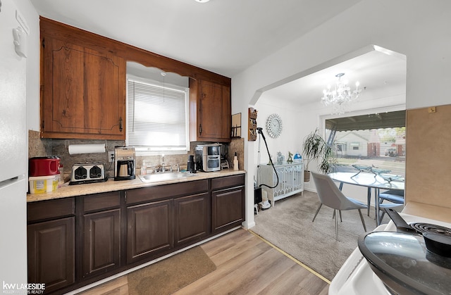 kitchen with pendant lighting, sink, tasteful backsplash, an inviting chandelier, and light hardwood / wood-style floors