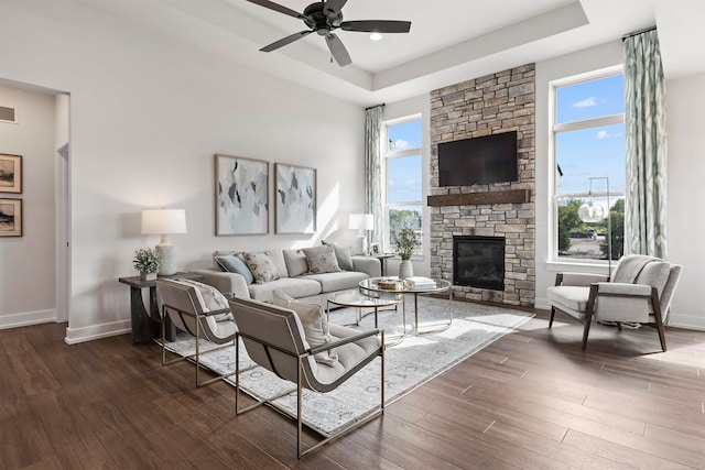 living room featuring ceiling fan, dark hardwood / wood-style floors, a tray ceiling, and a stone fireplace