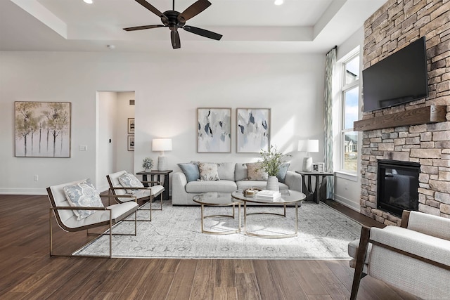 living room featuring a raised ceiling, ceiling fan, hardwood / wood-style floors, and a stone fireplace