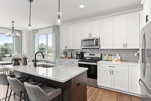 kitchen featuring decorative light fixtures, sink, stainless steel appliances, an island with sink, and white cabinets