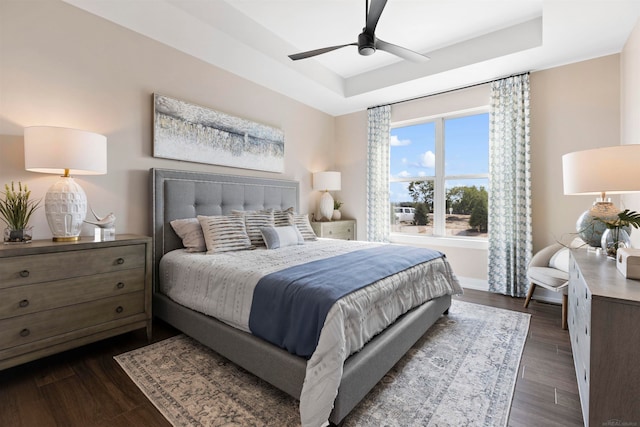 bedroom featuring dark wood-type flooring, a tray ceiling, and ceiling fan