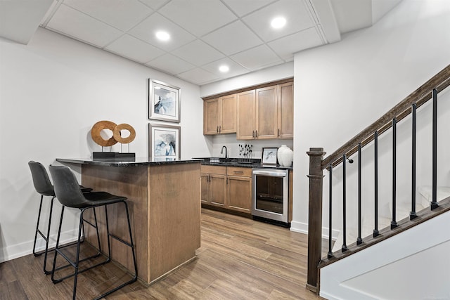 kitchen featuring sink, kitchen peninsula, beverage cooler, a kitchen breakfast bar, and light hardwood / wood-style floors