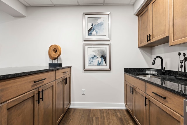 kitchen featuring a drop ceiling, dark stone countertops, sink, and dark hardwood / wood-style flooring