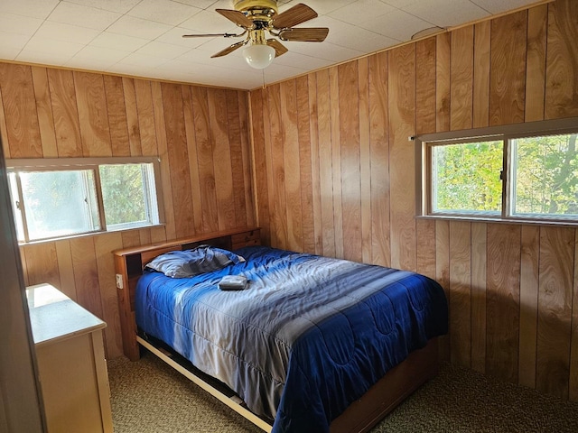 bedroom featuring multiple windows, ceiling fan, carpet floors, and wooden walls