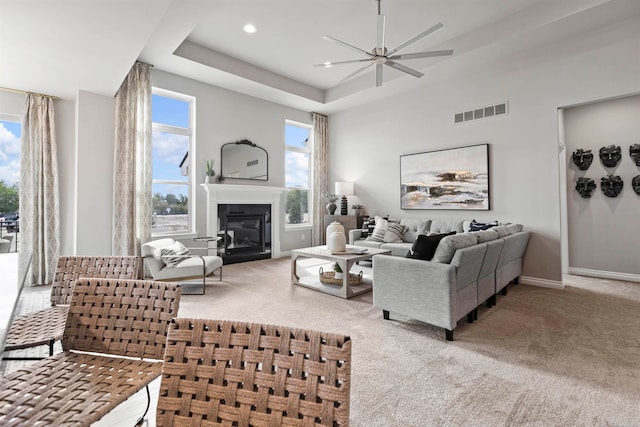 living room with ceiling fan, carpet floors, and a tray ceiling