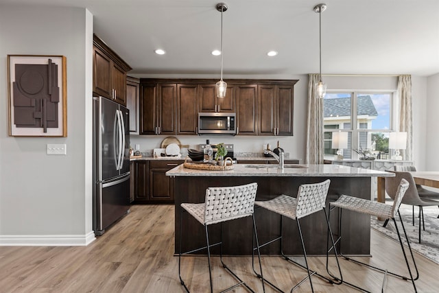 kitchen featuring light hardwood / wood-style floors, a kitchen island with sink, pendant lighting, light stone counters, and appliances with stainless steel finishes