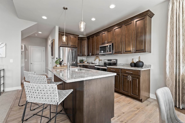 kitchen featuring light stone counters, stainless steel appliances, light hardwood / wood-style floors, pendant lighting, and dark brown cabinets