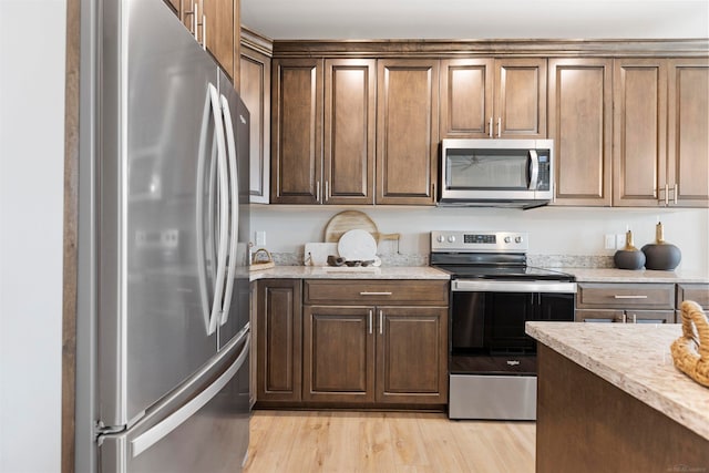 kitchen with appliances with stainless steel finishes, light stone counters, and light hardwood / wood-style flooring