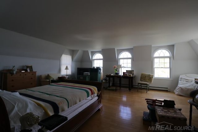 bedroom featuring hardwood / wood-style flooring, vaulted ceiling, and a baseboard heating unit