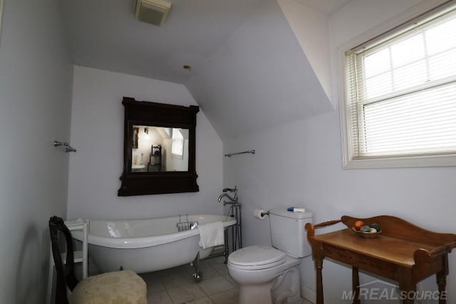 bathroom with vaulted ceiling, tile patterned floors, toilet, and a tub